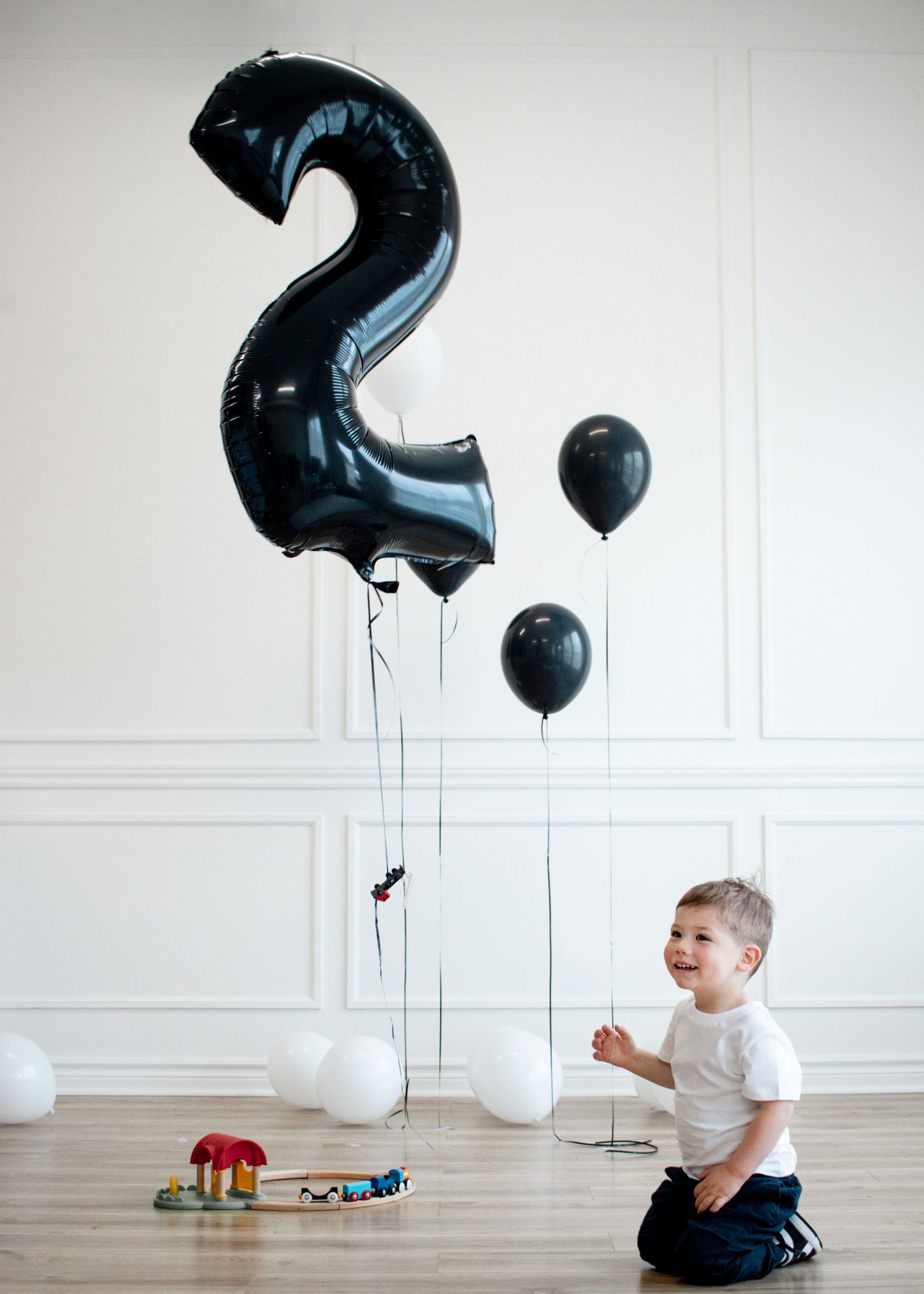 Two year old with a black number 2 balloon and a train set