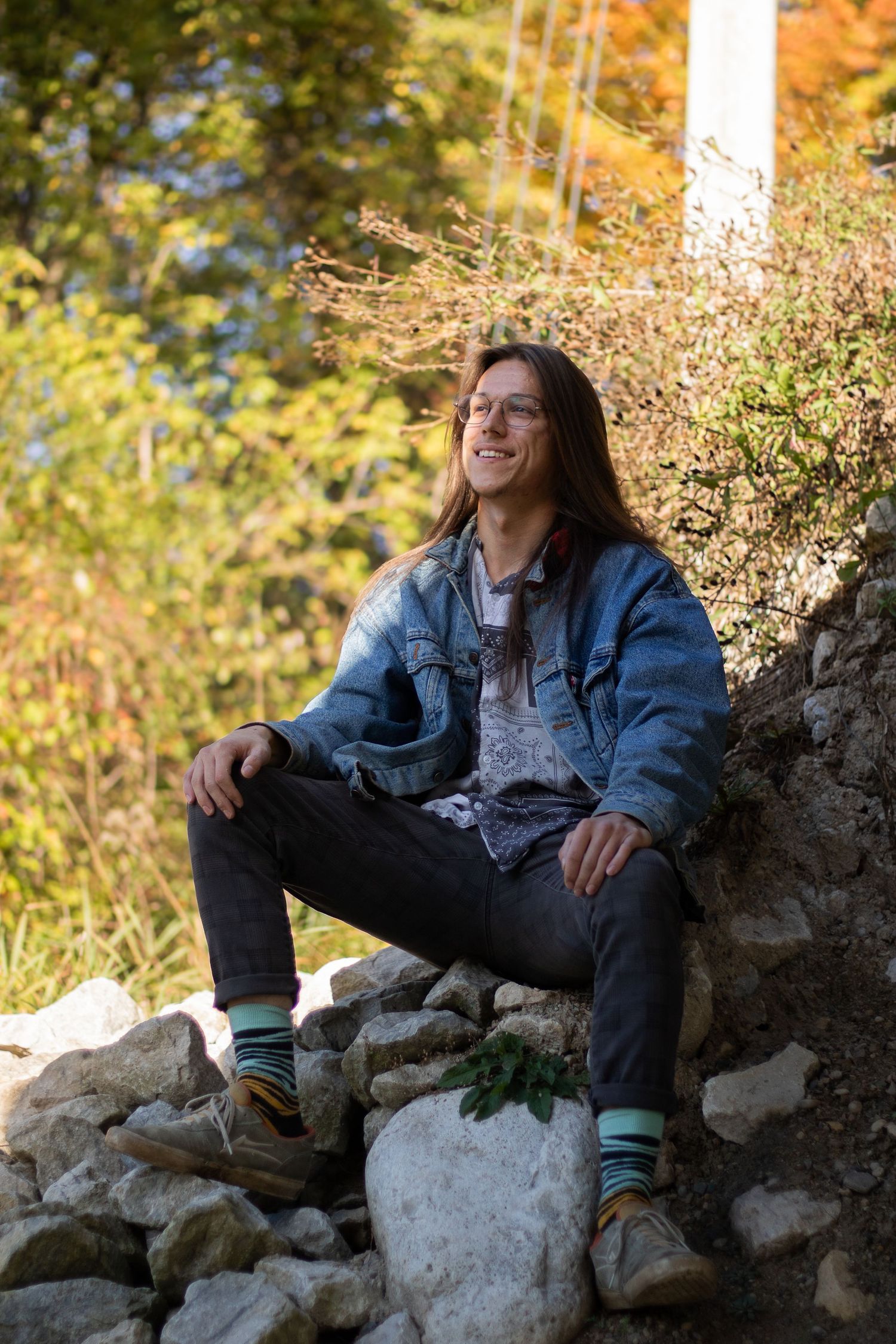 Young man with long hair sitting in the shade under a bridge