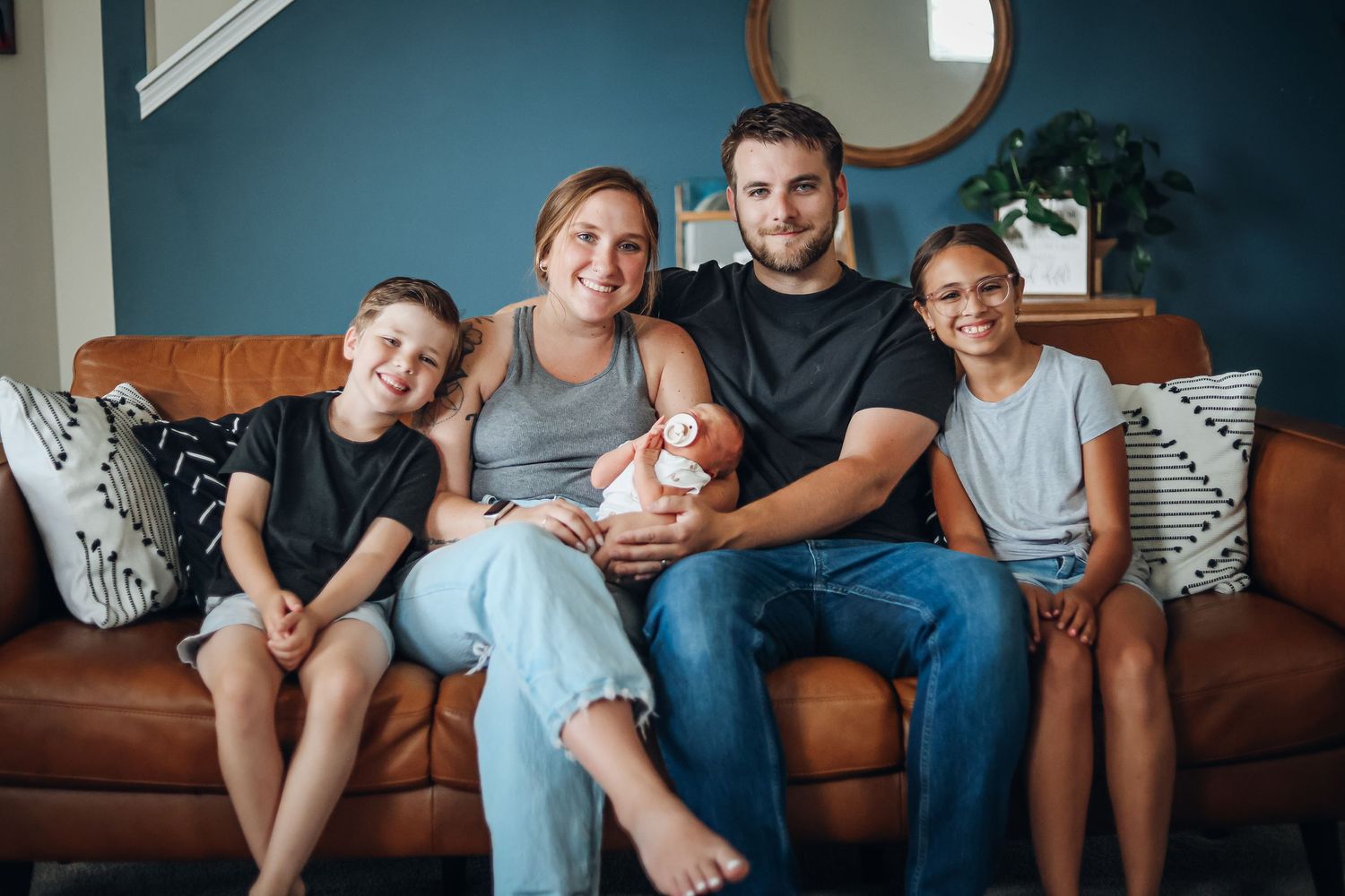 Family gathering on blue couch in living room with natural lighting. Example of family style newborn photography
