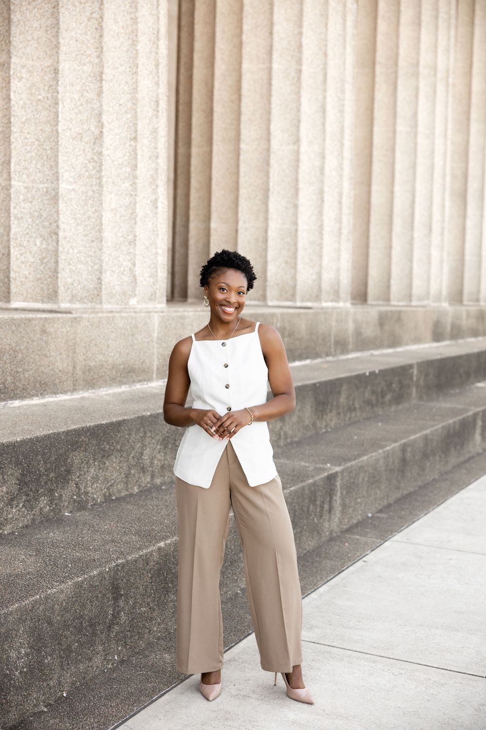 Professional fashion photo showing a white sleeveless top paired with beige wide-leg pants against a columned backdrop.
