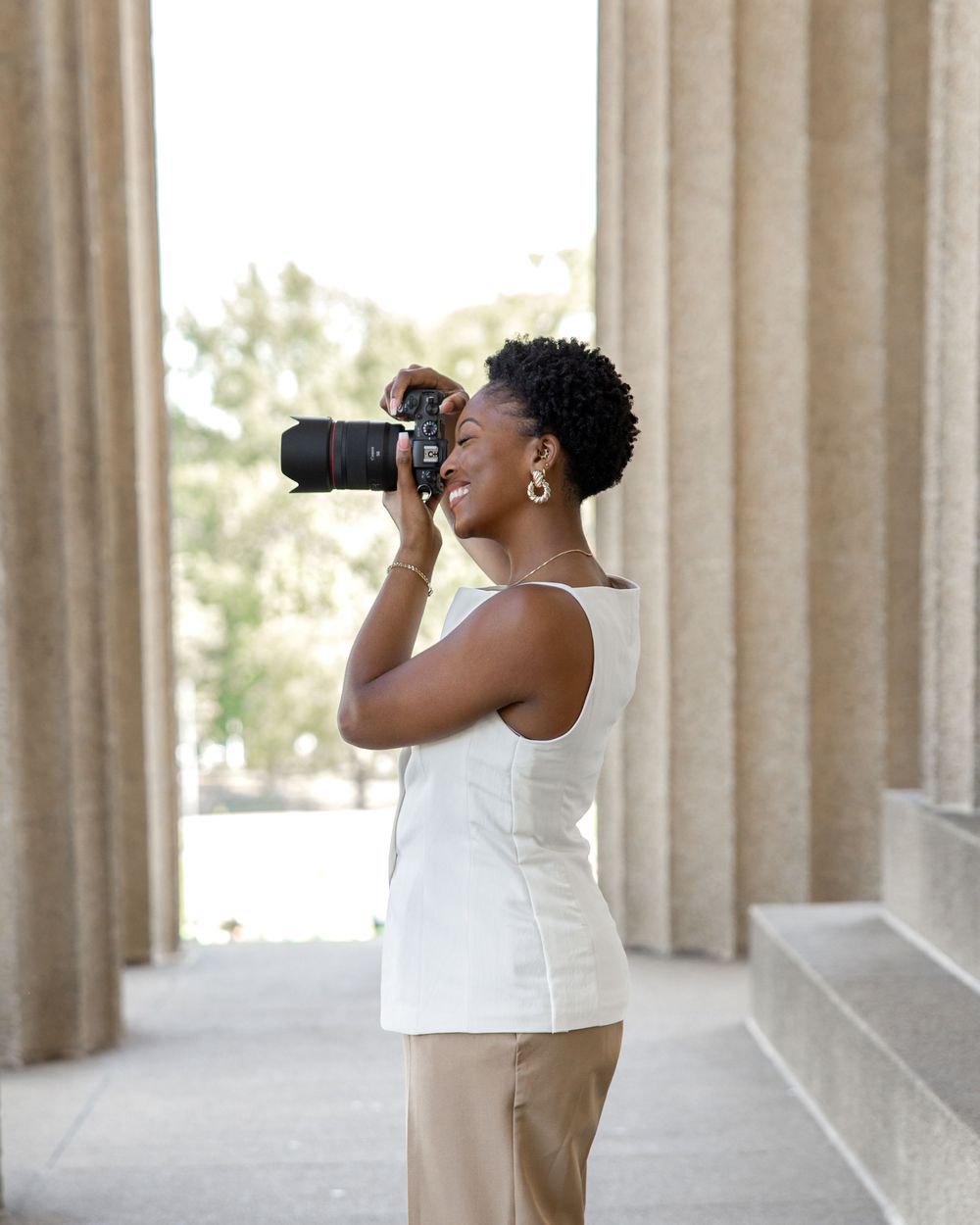 A person in a white sleeveless top drinks from a water bottle while standing in front of stone columns.
