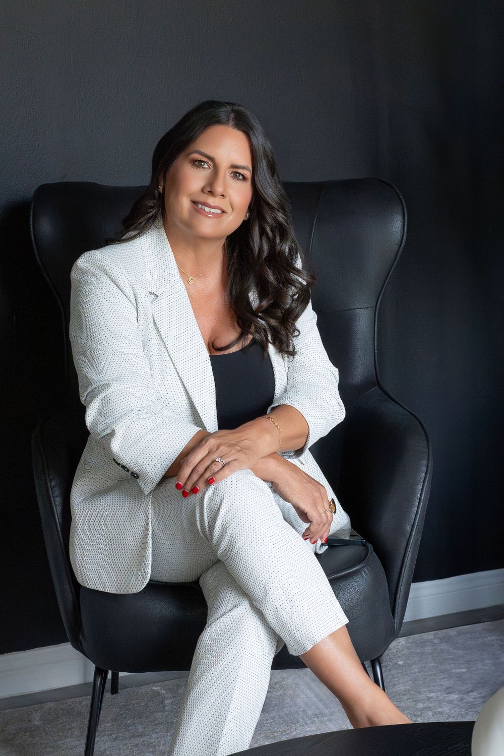 Portrait of person in white suit seated elegantly in black leather chair.