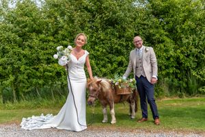 Bride and groom take wedding photos with their brown horse on a path surrounded by lush greenery.