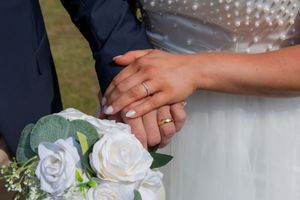 Newlyweds holding hands showing wedding rings with a white rose bouquet at their wedding ceremony.