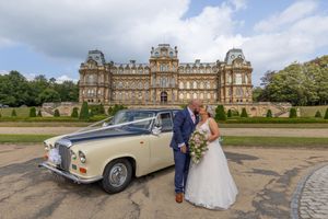 Elegant vintage cream-colored Bentley wedding cars parked outside a grand historic manor house.