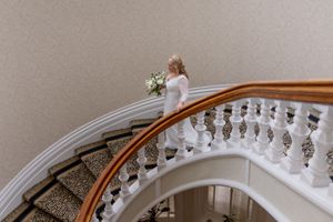 Elegant curved staircase with white marble balusters and polished wooden handrail in a wedding venue setting.