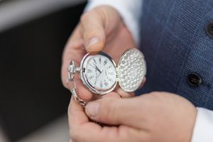 Close-up of hands holding an ornate silver pocket watch with a decorative engraved cover.