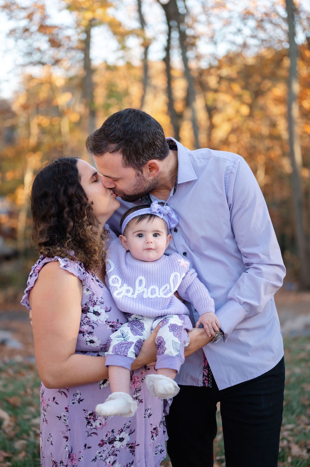 A family with a baby having a tender moment during an autumn photo session in the woods.