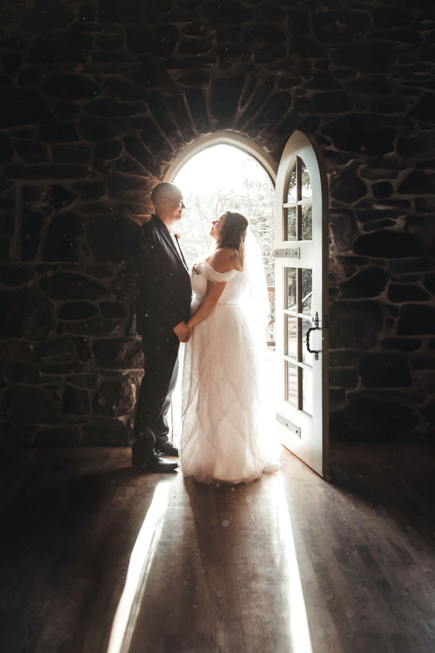 Silhouette of wedding couple standing in doorway with bright backlight through stone archway.