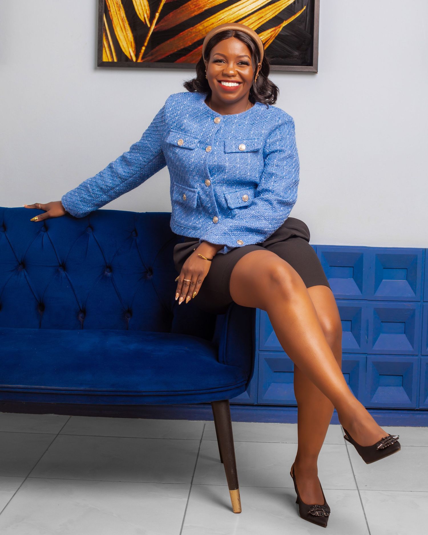 A person in a denim shirt poses confidently on a royal blue velvet couch in a professional studio setting.