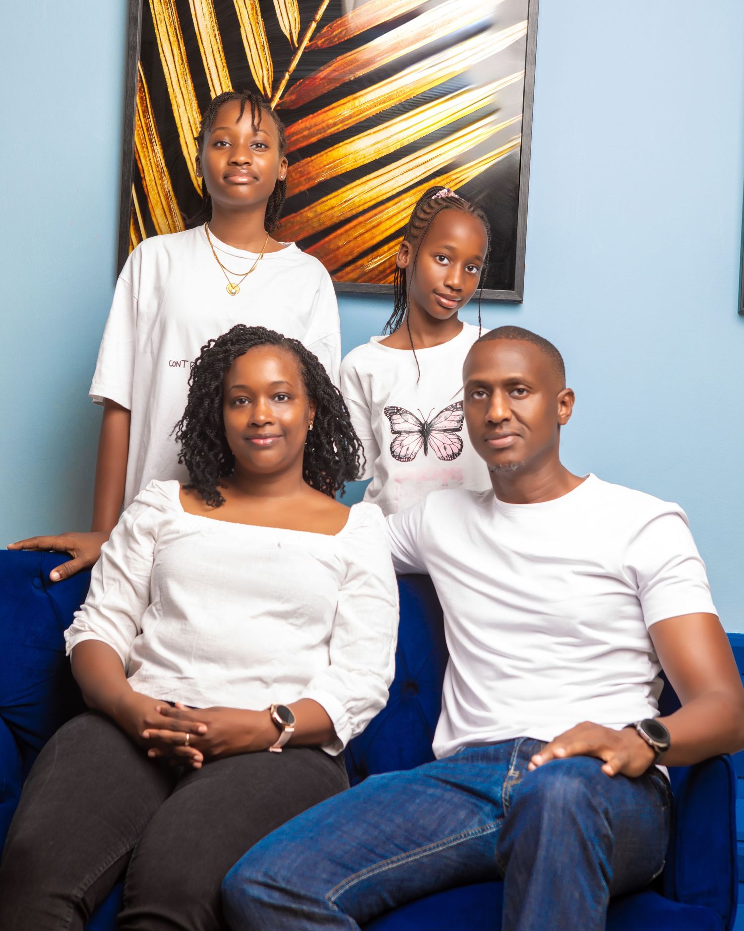 A family wearing coordinated white tops and blue jeans poses together against a wall with colorful artwork.