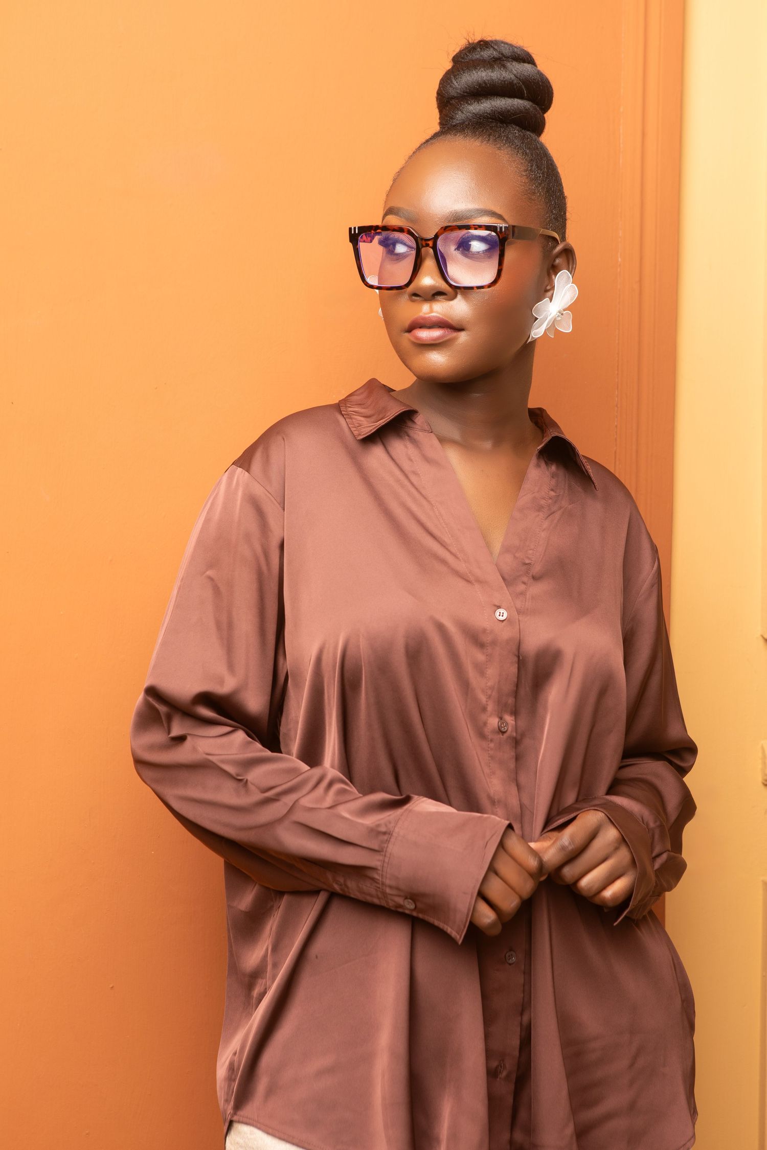 A series of fashion photos showing brown oversized sweatshirts styled with glasses and accessories against an orange wall.