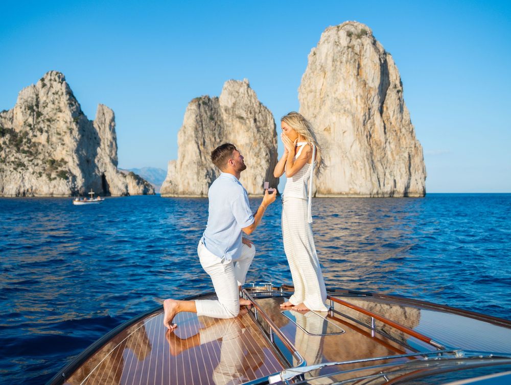 A couple enjoys a romantic boat ride near the iconic Faraglioni rock formations off the coast of Capri, Italy.