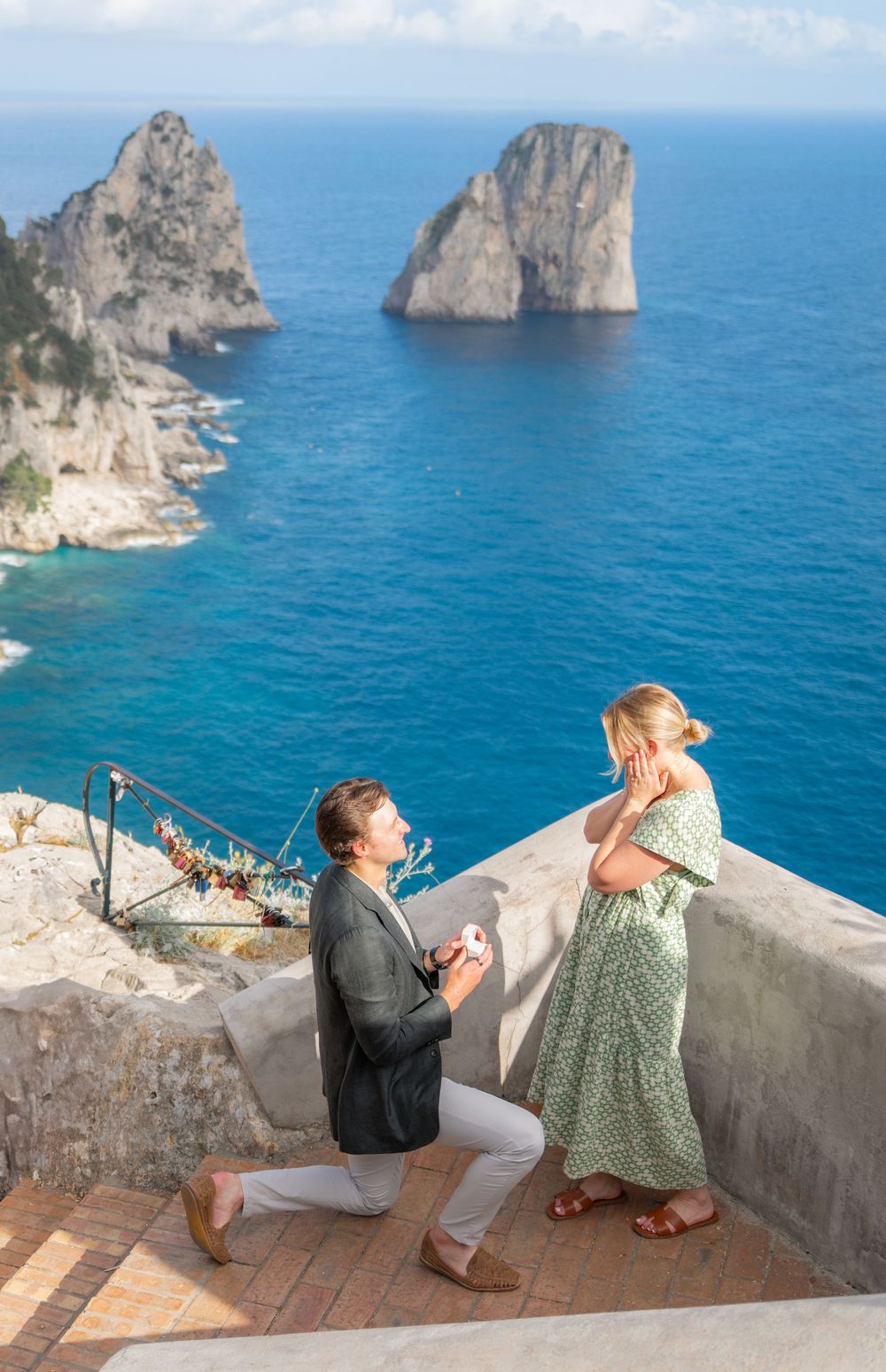 A romantic proposal moment unfolds on a scenic terrace overlooking the famous Faraglioni rocks of Capri, Italy.