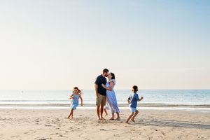 A family enjoys a playful moment together while walking along a sunny beach at sunset.