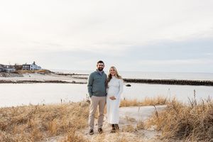 A couple walks along a serene coastal path with tall grass and ocean views on a cloudy winter day.