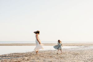 Two figures in flowing dresses dance together on a serene beach at sunset.