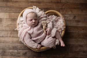 Sleeping newborn baby wrapped in soft pink swaddle blanket lying in wooden basket against rustic background.