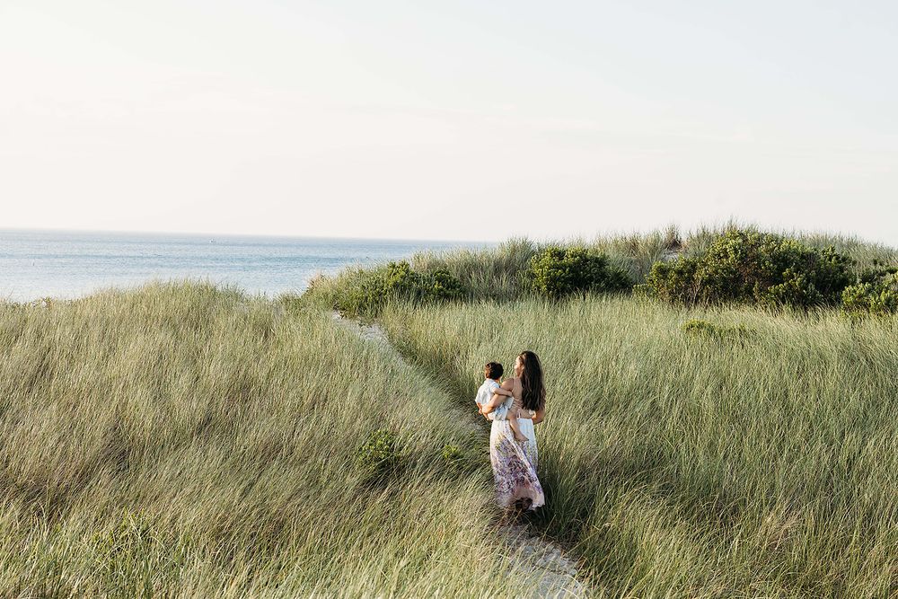 Couple walking together through tall grass on a scenic coastal path with ocean views in the background.