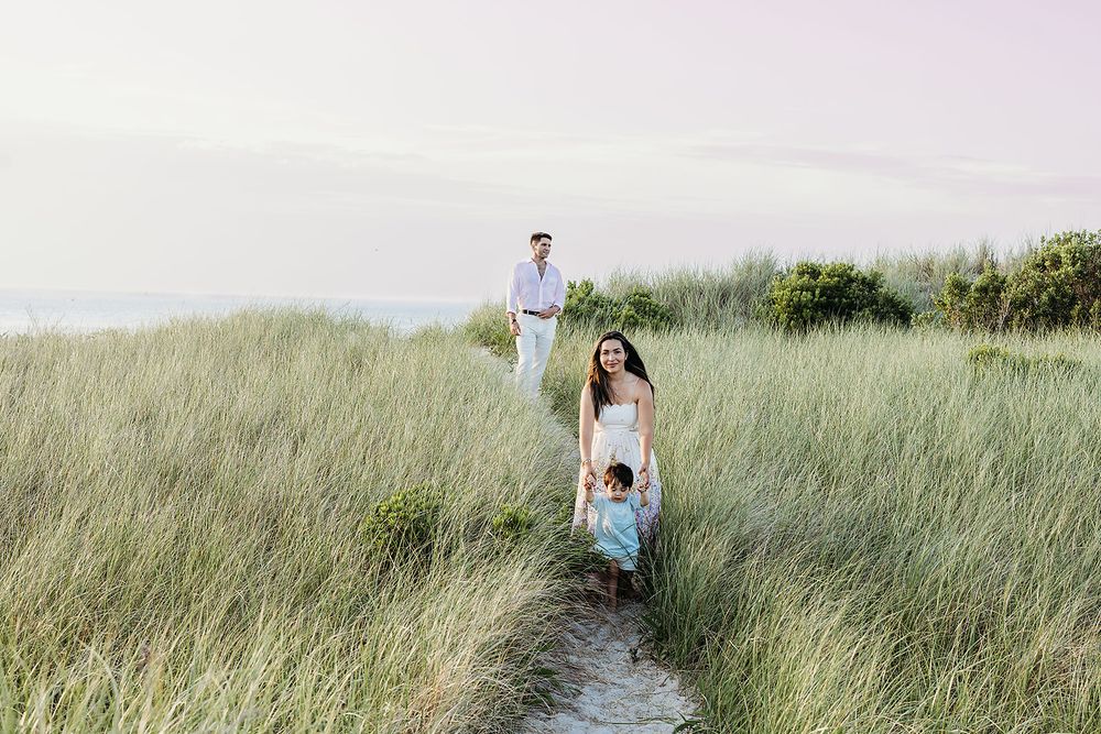 A couple walks through tall grass in a field at sunset, creating a romantic silhouette against the golden sky.