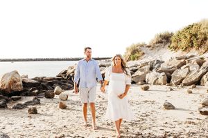 A happy couple enjoys a romantic photoshoot on a scenic beach with rocky cliffs and golden sunlight.
