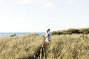 A person walks along a grassy coastal hillside path against a bright blue sky on a sunny day.