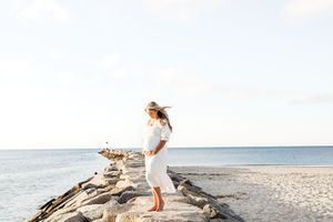 A person in white summer attire walks along a pristine beach shoreline with waves and blue sky in the background.