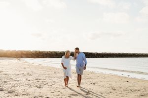 Two people walk hand in hand along a serene beach at sunset, leaving footprints in the white sand.