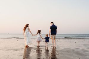 Family holding hands while walking together on a sandy beach at sunset with ocean waves in background.