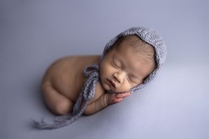 A sleeping newborn baby swaddled in soft gray fabric lies peacefully against a light background.