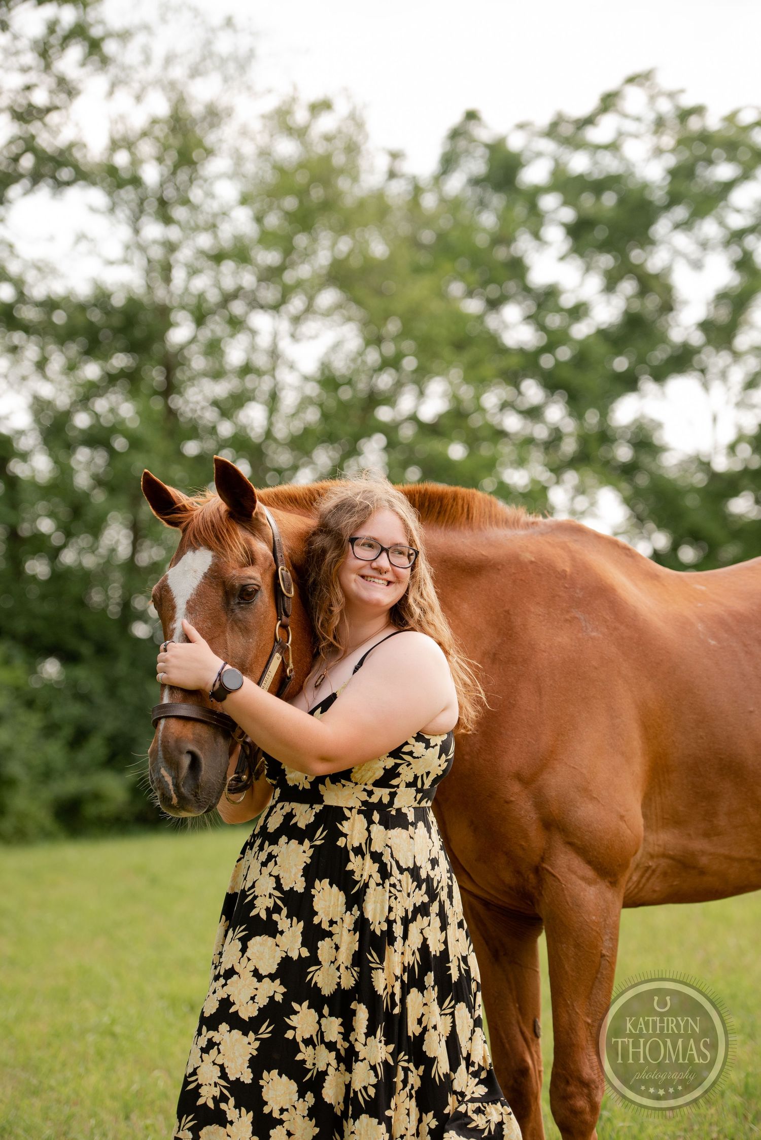 A beautiful chestnut horse poses with its handler in a floral dress outdoors.
