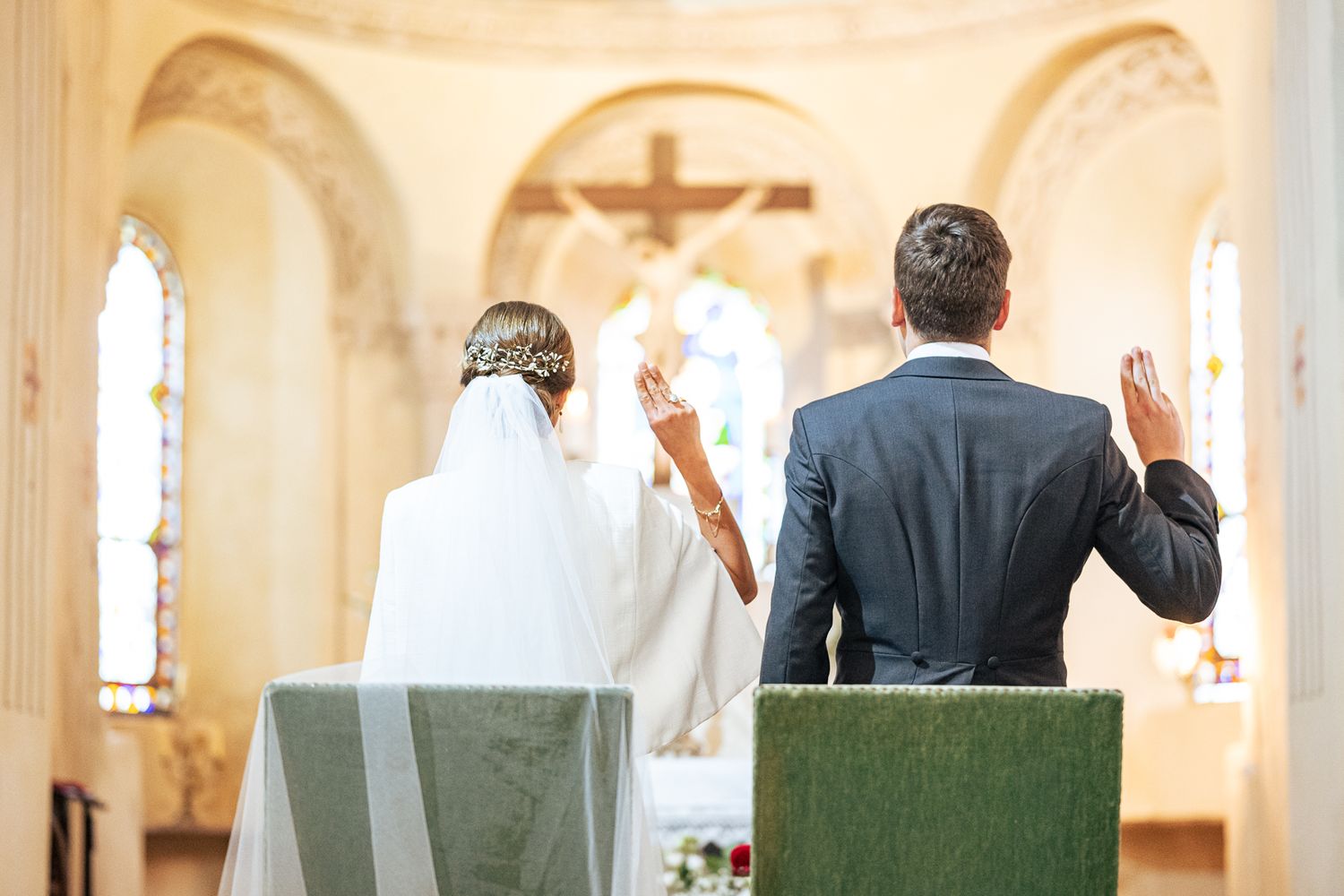Two people stand with raised hands during a religious ceremony in a church with a cross visible.