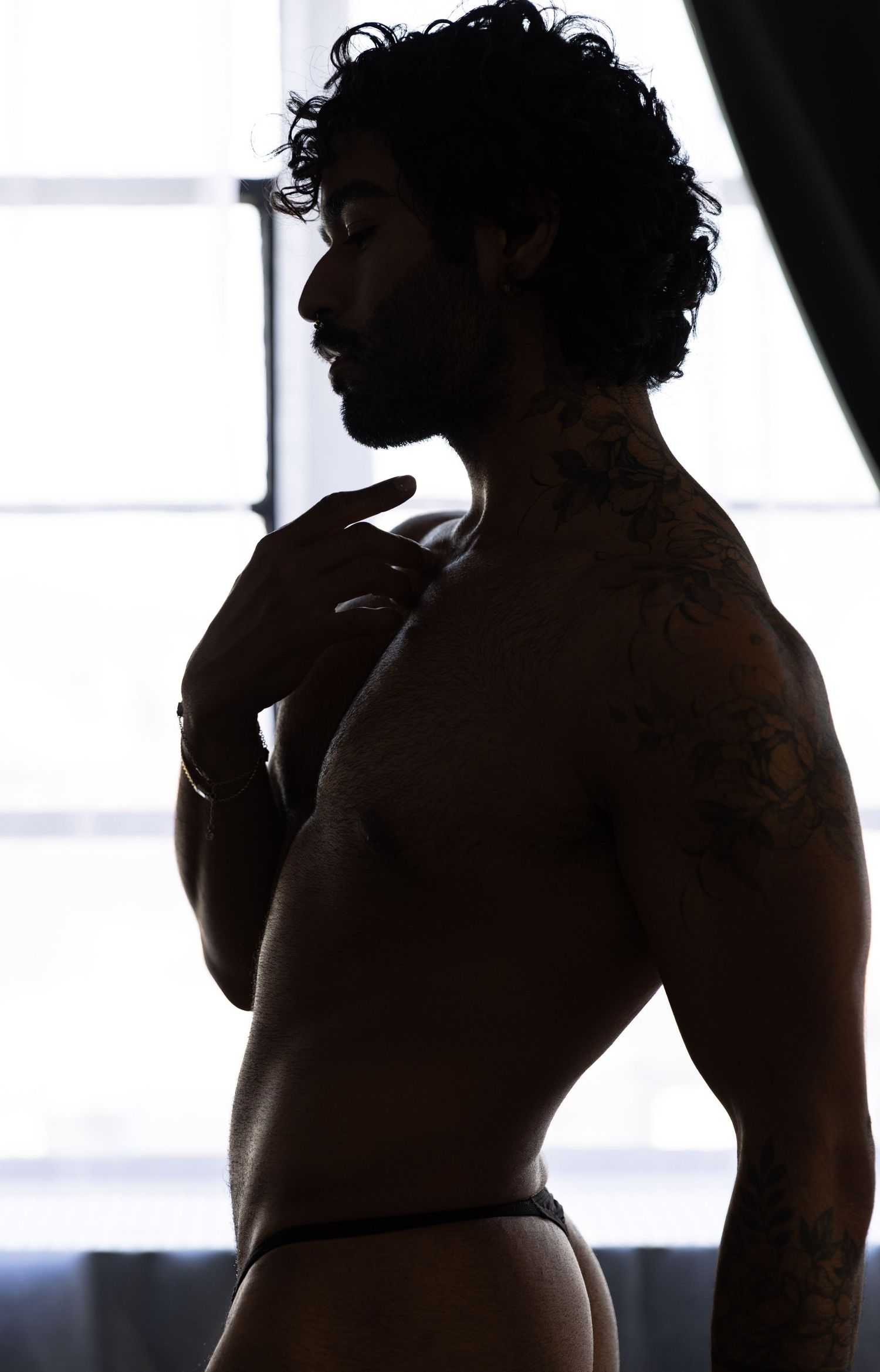 Photograph of shirtless man in underwear standing in front of window by Los Angeles boudoir photographer.