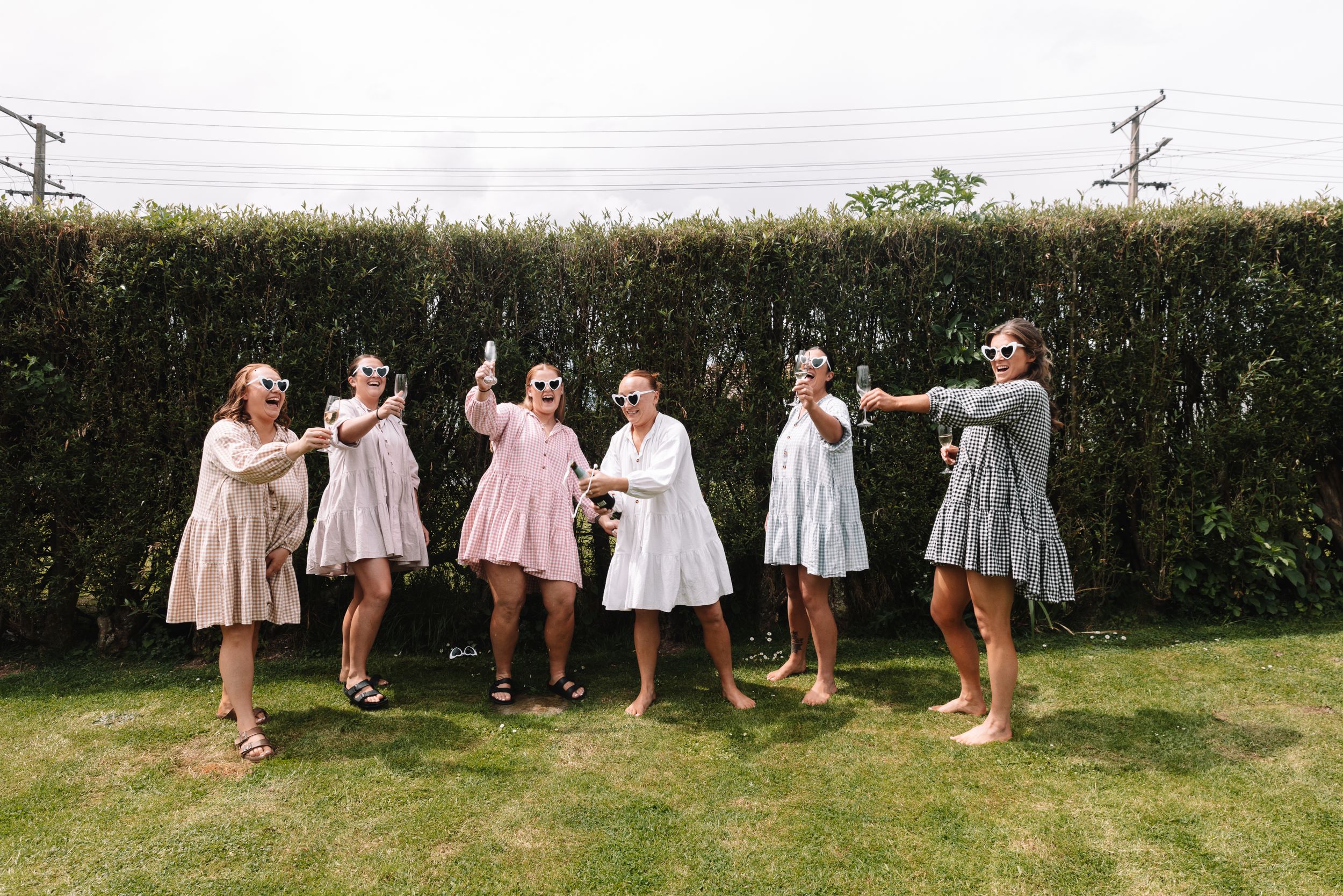 A group of women in vintage-style dresses posing playfully in a garden setting.