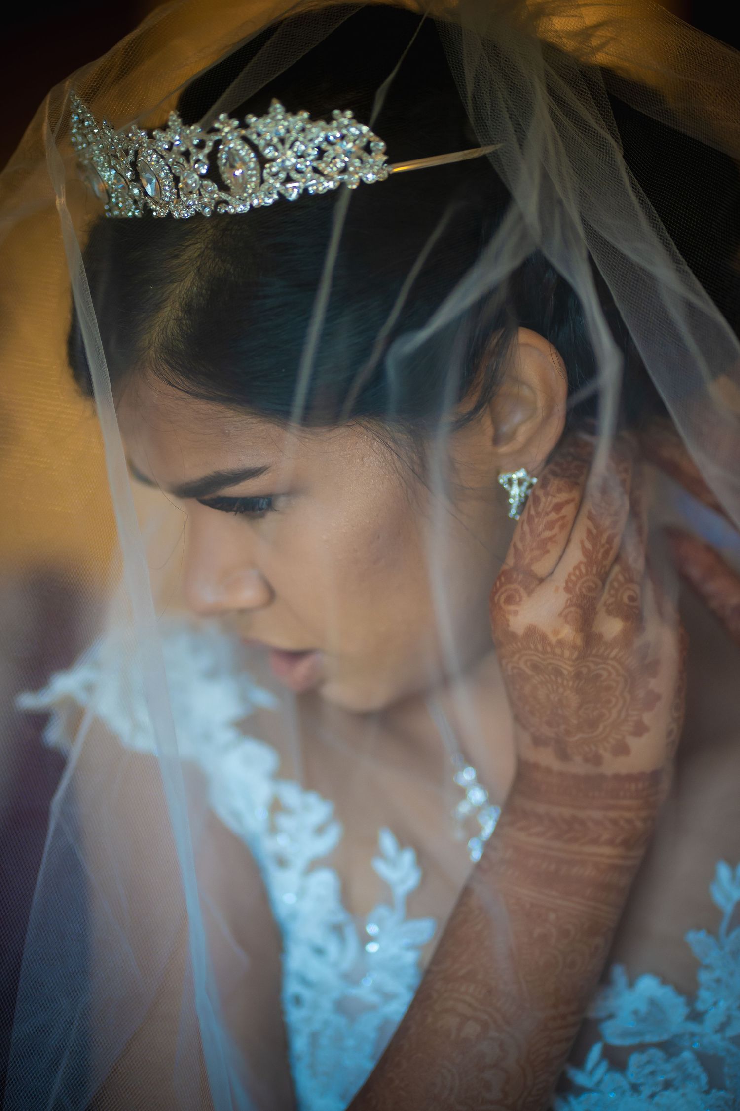 Bride covered in a thin veil puts on her silver earring. Her hand has beautiful henna tattoos