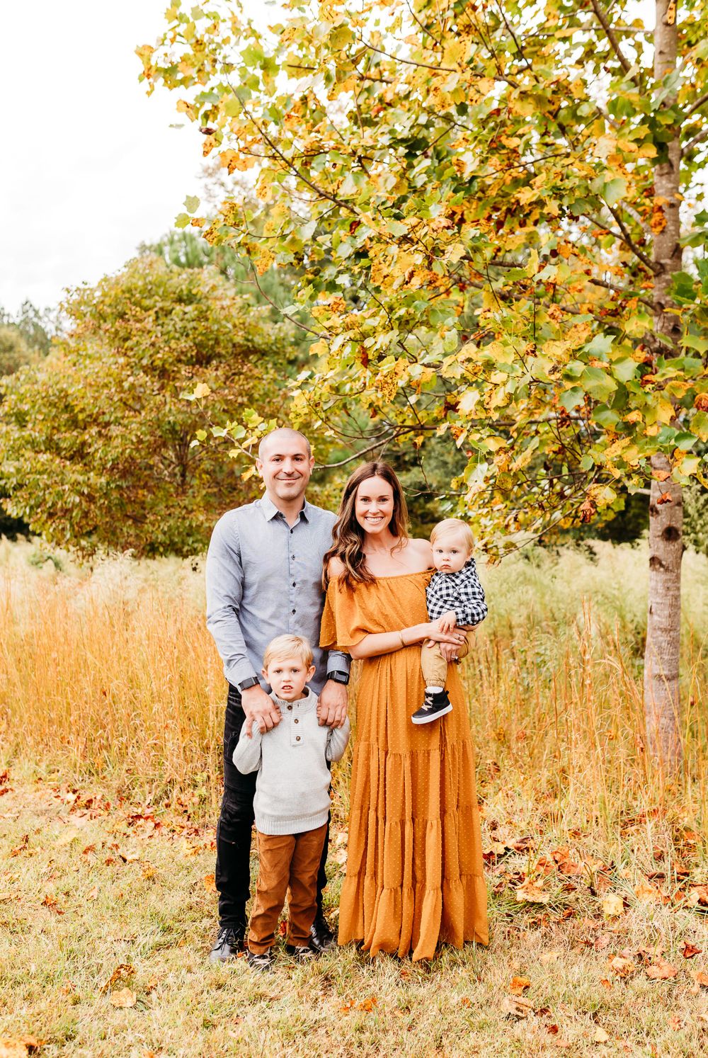 A group poses together in a fall setting with golden leaves and tall grass in the background.