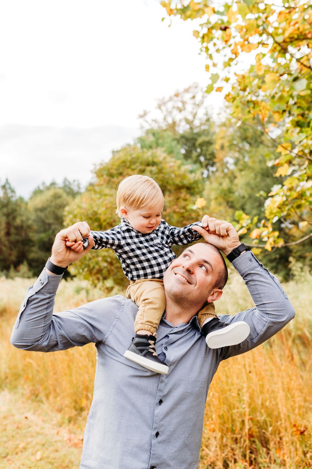 A parent and child playing together in a golden autumn field with yellow leaves and tall grass.