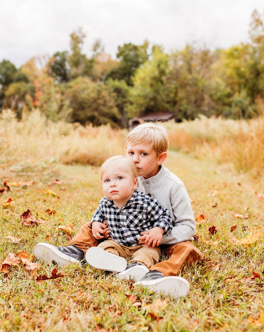 A child lies in a grassy field with autumn leaves scattered around during a golden sunset.