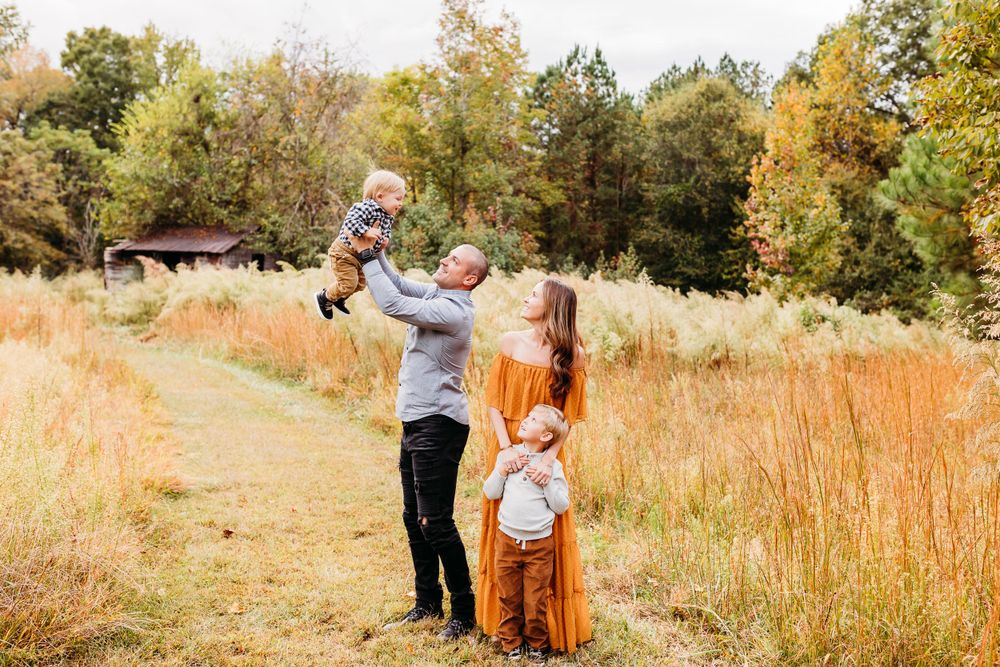 A family enjoys a warm autumn day together in a golden field surrounded by tall grass and trees.