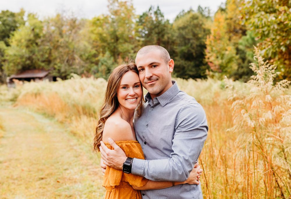 A couple shares a tender moment in a golden autumn field during sunset with tall grass surrounding them.
