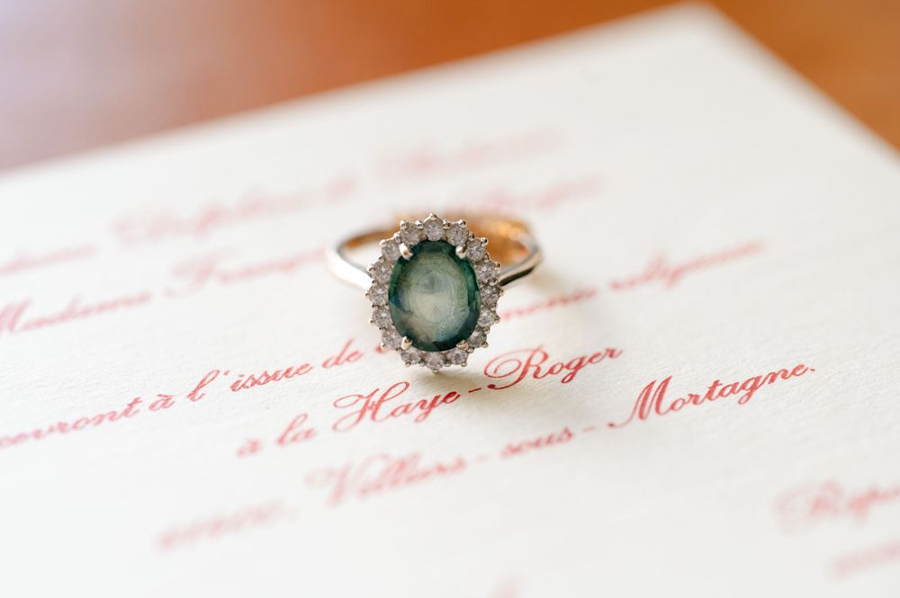 Vintage style engagement ring with green gemstone sitting on pink text document.