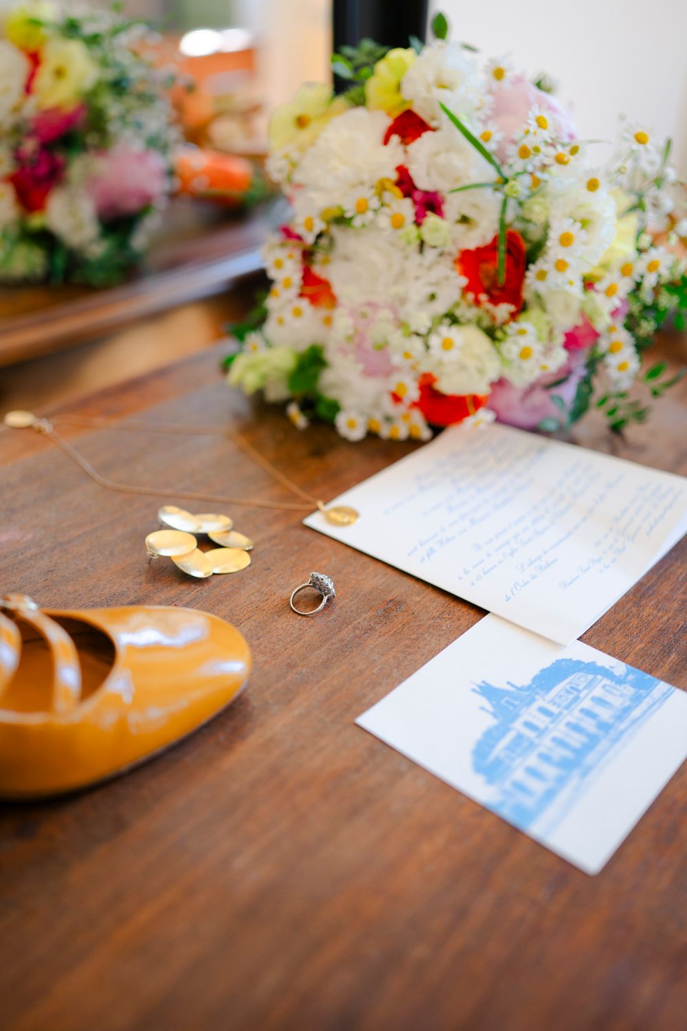 Wedding details arranged on a wooden table with colorful flowers, blue stationery and rings.