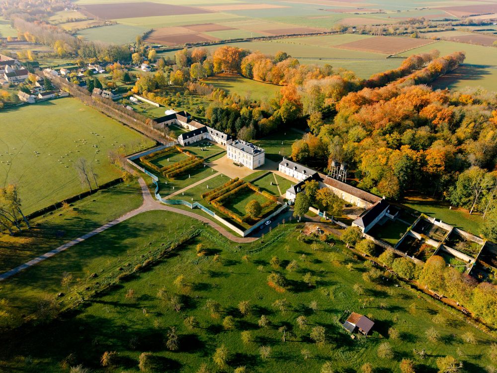 Aerial drone view of rural farmland with autumn trees and scattered buildings in golden afternoon light.