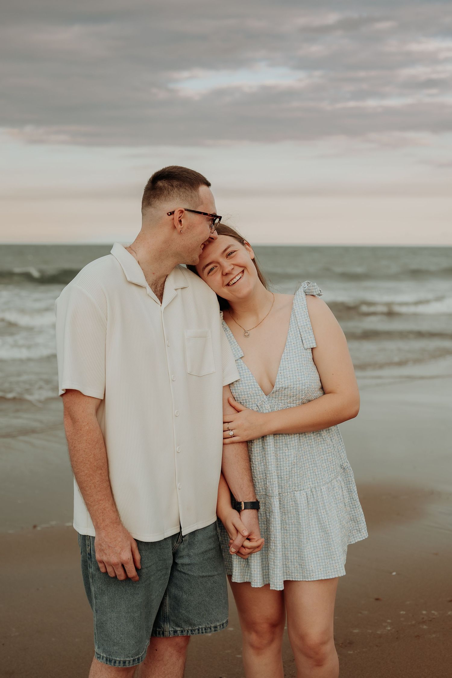 Romantic couple embracing on a cloudy gladstone beach at sunset.