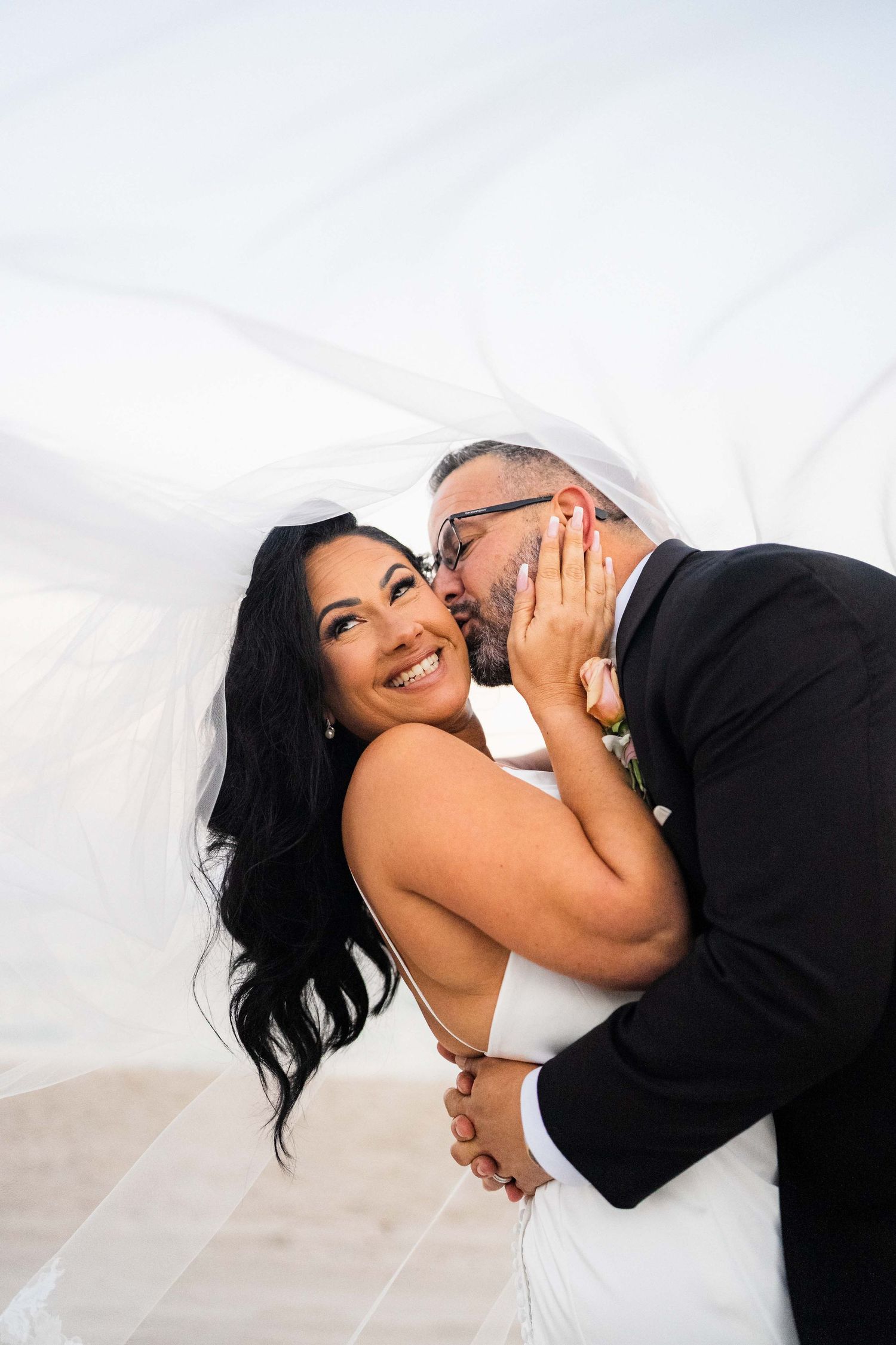 Joyful wedding moment captured against a bright sky with flowing veil.