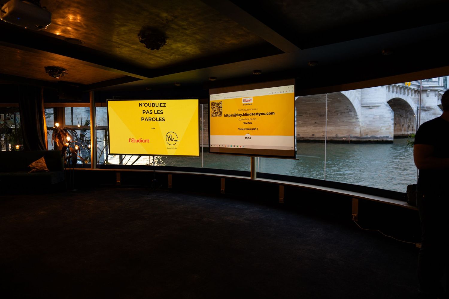 Dual yellow screens display information inside a dark exhibit space with curved walls overlooking water.
