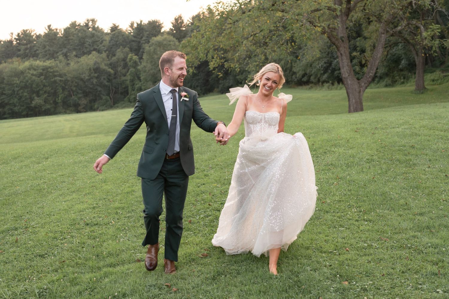 Happy couple runs through grassy field during sunset wedding photo.