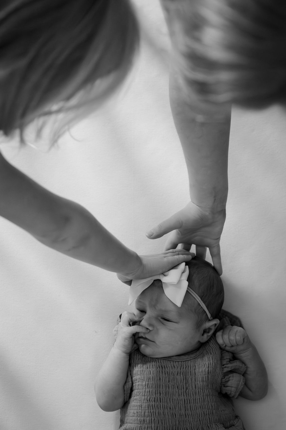 Black and white photo of mother gently touching sleeping newborn baby girl with bow headband.