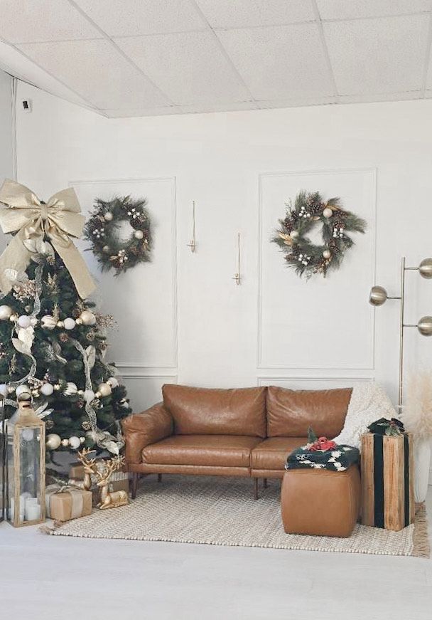 Family dressed in neutral tones posing for holiday photos in front of decorated Christmas tree.
