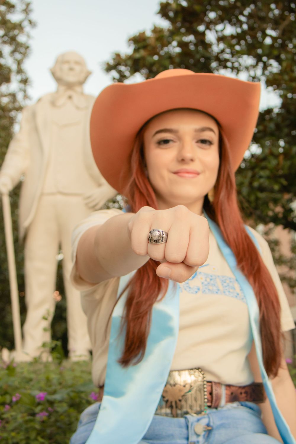 Sam Houston State University graduate showing off her class ring in front of a statue of Sam Houston.